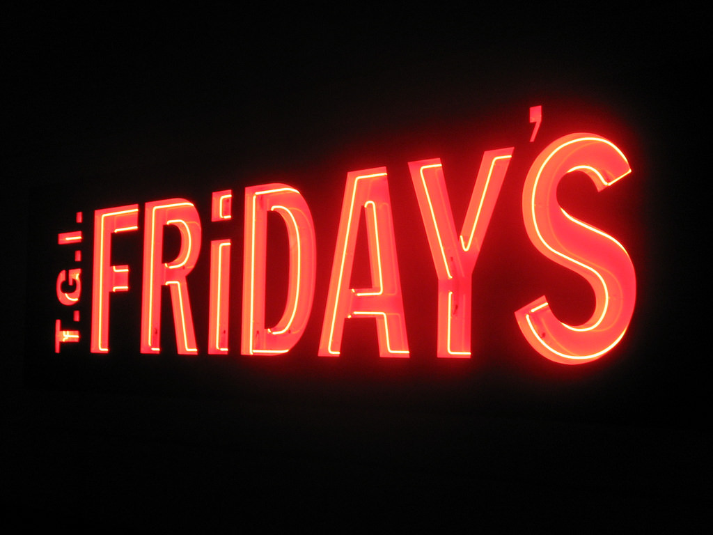 TGI Fridays sign lit up in neon orange against a dark black background