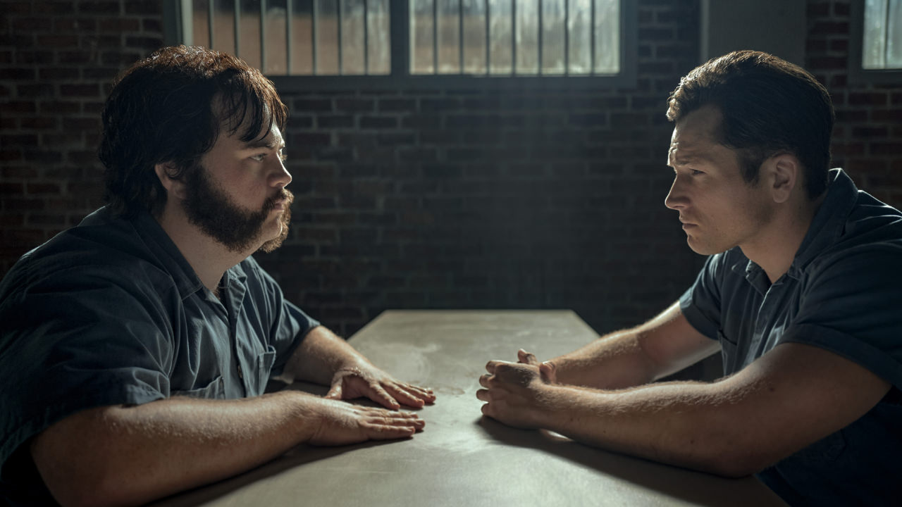 A still from the TV show Black Bird featuring Taron Egerton and Paul Walter Hauser sitting opposite each other at a table in prison