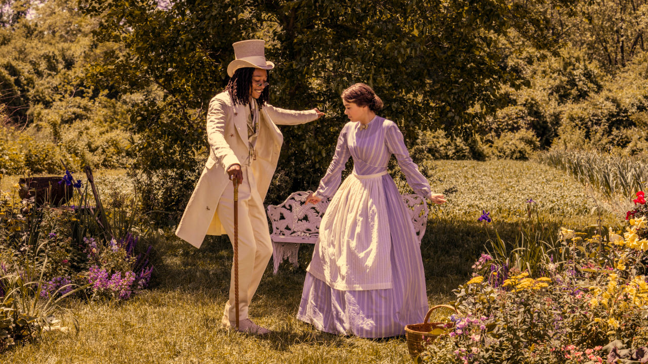 A still image from Dickinson series 3, episode 10 showing Hailee Steinfeld (Emily Dickinson) and Wiz Khalifa (Death) dancing in a springtime garden