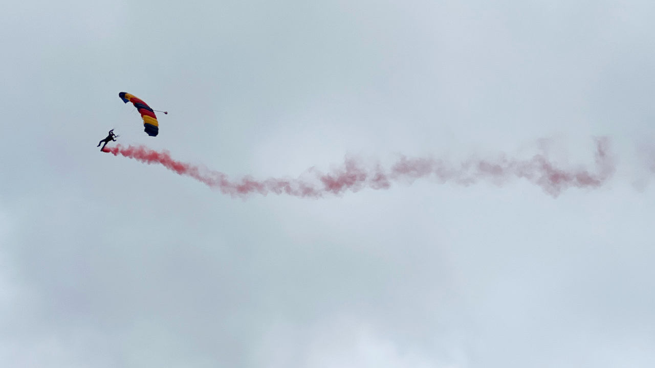 One member of a parachute display team descending towards the earth streaming red smoke behind him