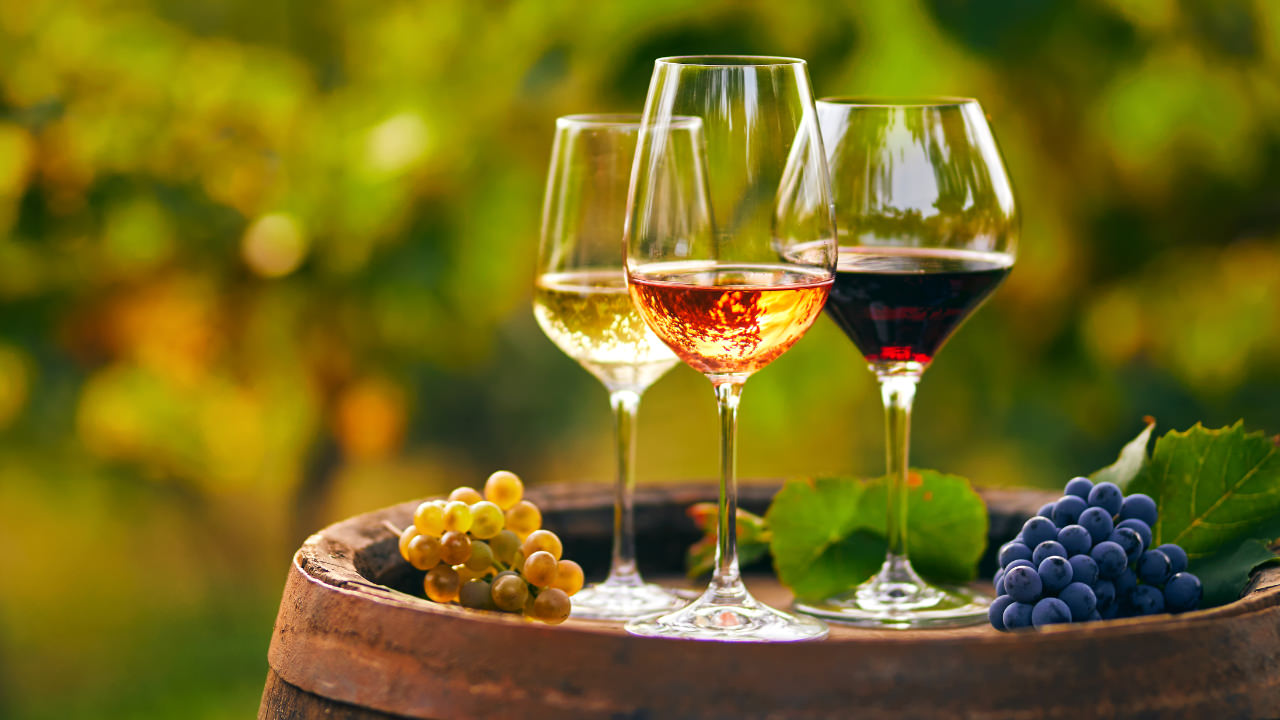 Three wine glasses and some grapes on a wine barrel in the sunshine
