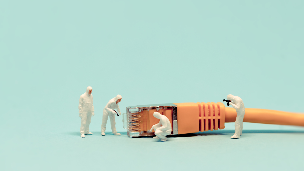 An orange network cable with miniature figures in white coveralls inspecting it, one with a camera pressed to their eye