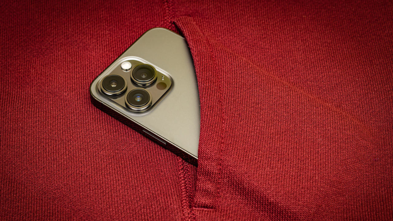 An Apple iPhone tucked into the pocket of a garment made of red wool, laying flat on a surface