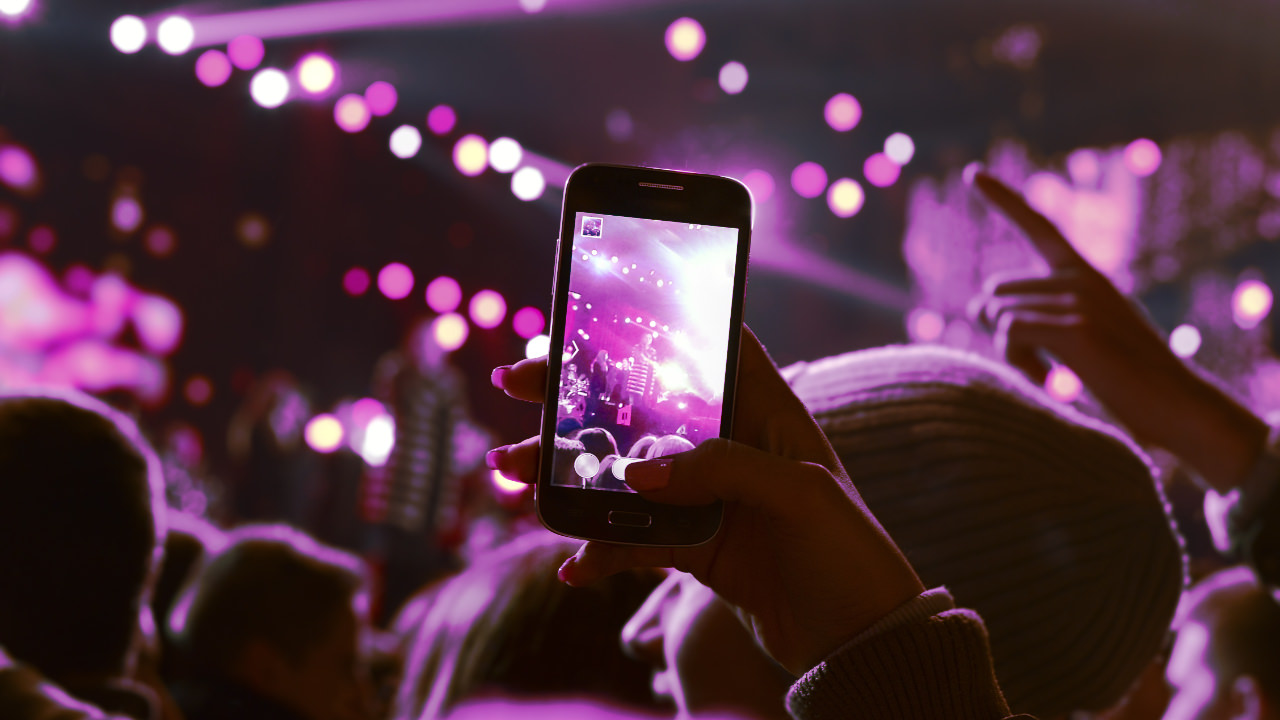 From the point of view of someone at a gig, holding up their phone to capture the artist on stage, with a purple filter on top