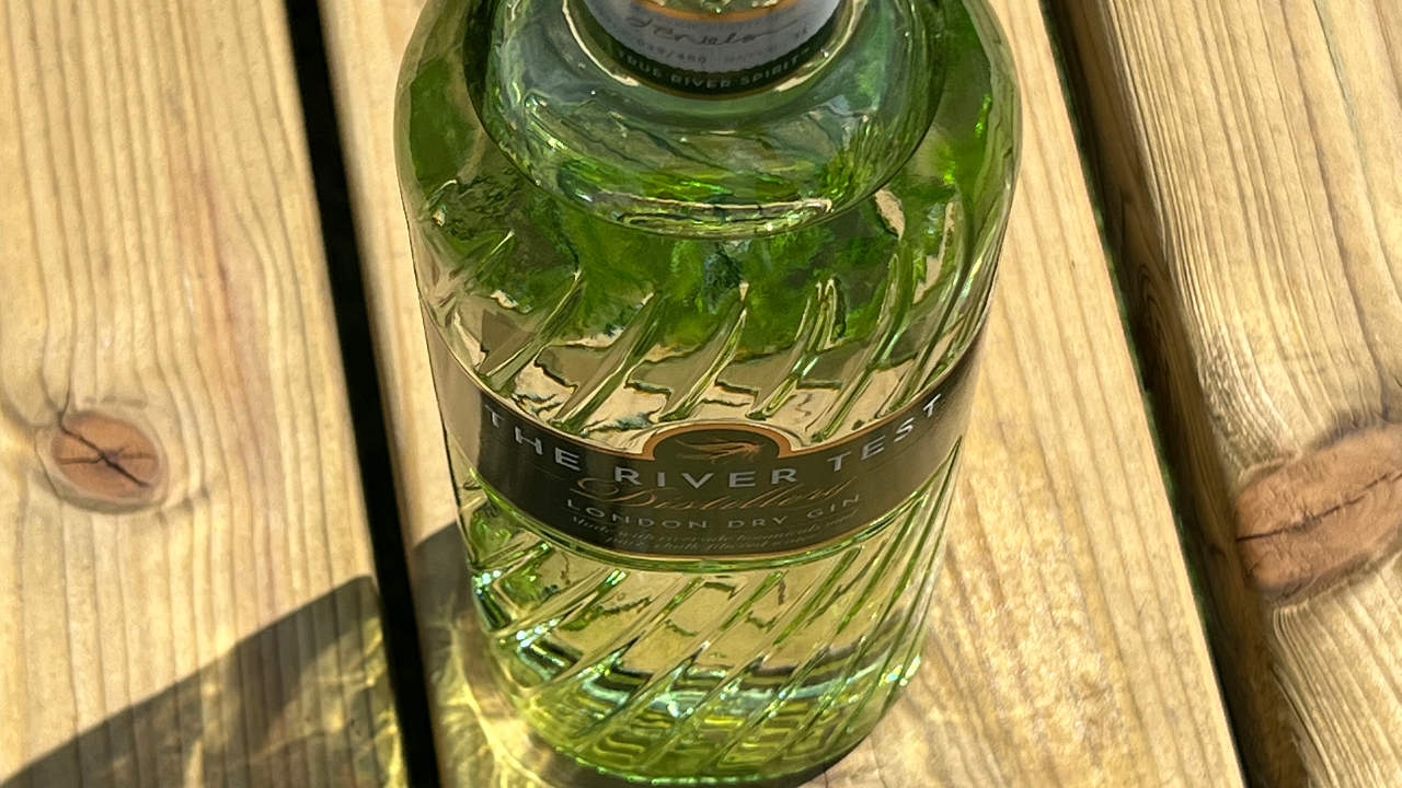 Looking down on a green gin bottle of The River Test gin sitting upon a brown picnic table
