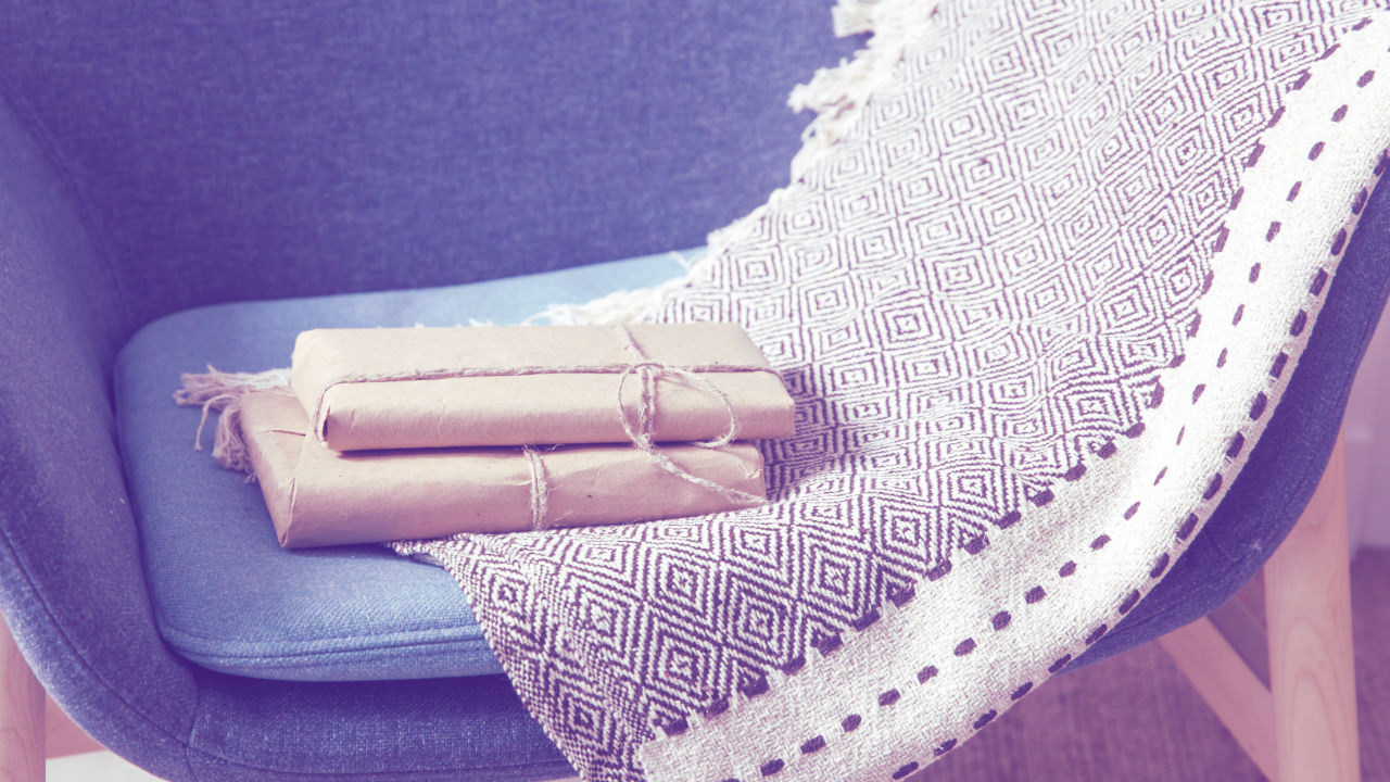 Two books wrapped in brown paper and tied with string, placed on a blue chair with a blanket draped to one side