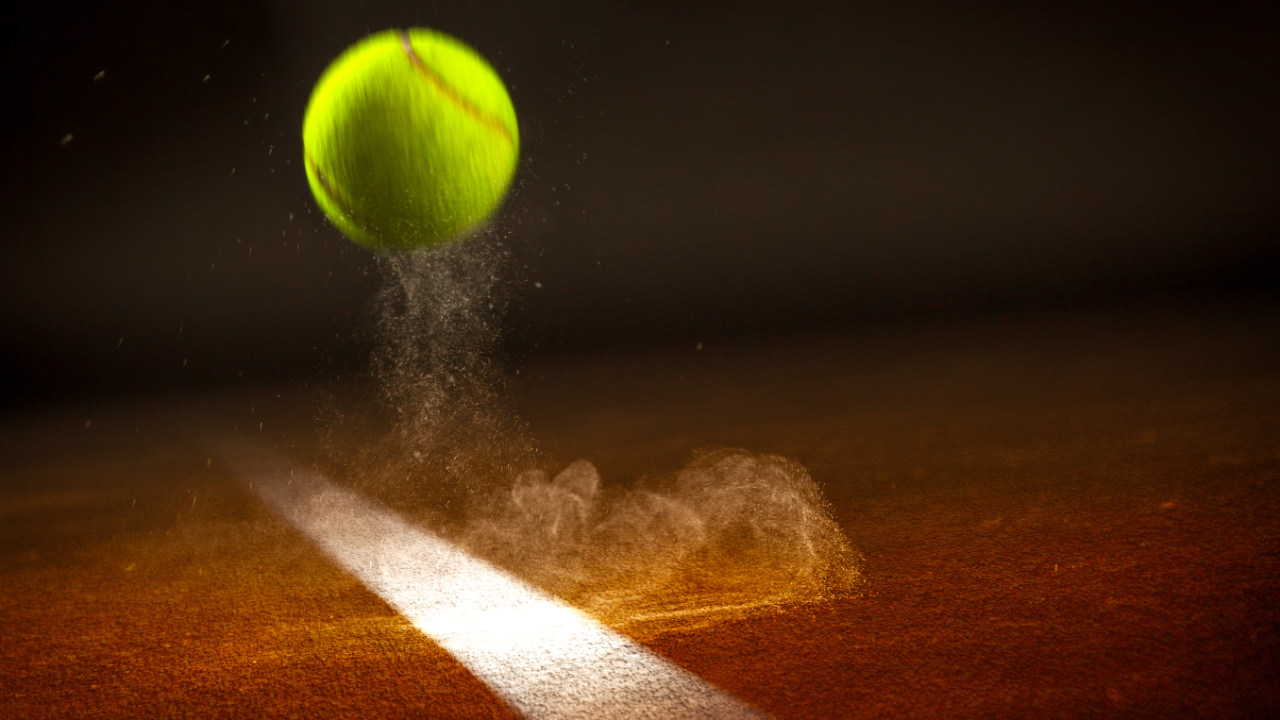 A tennis ball bouncing off the line on a clay court, with a puff of clay in the air