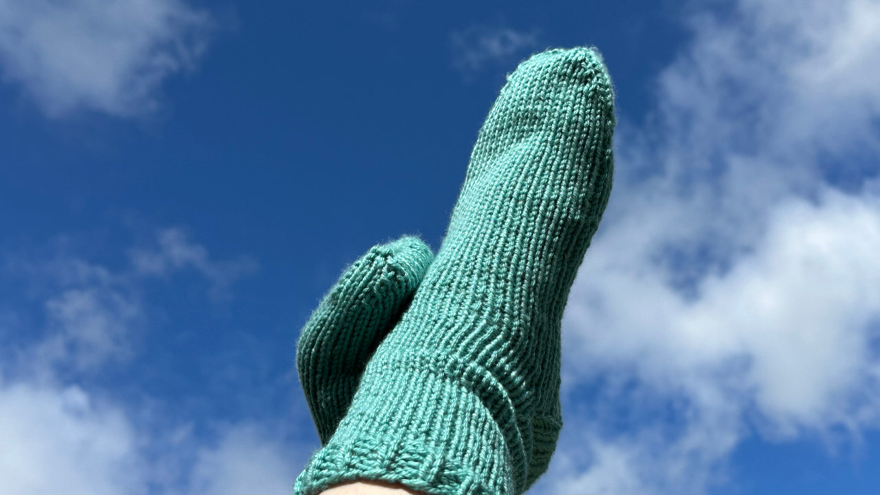 A photograph of feet against a blue and cloudy sky, with green knitted socks on display