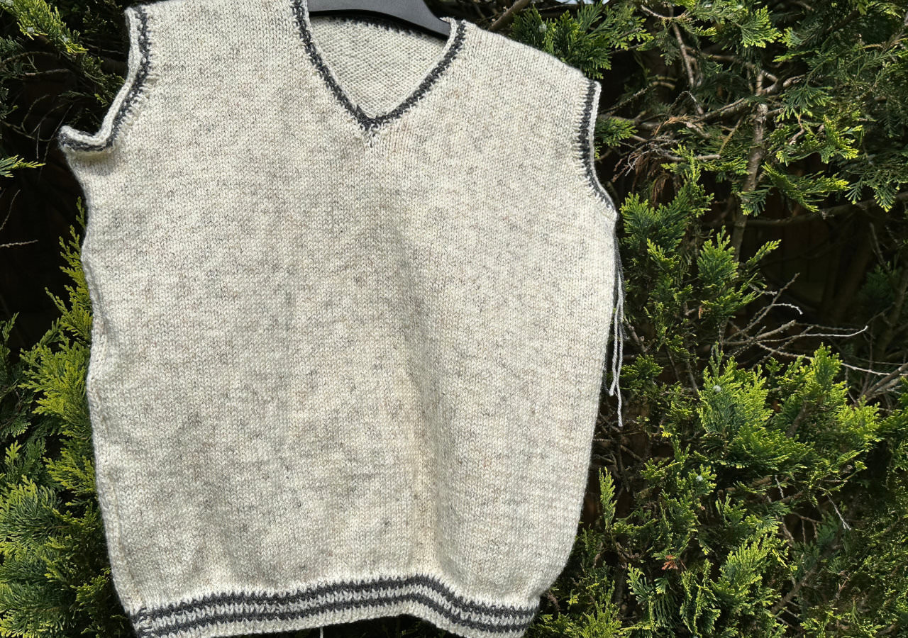A photograph of a knitted v-neck vest, white with grey edging