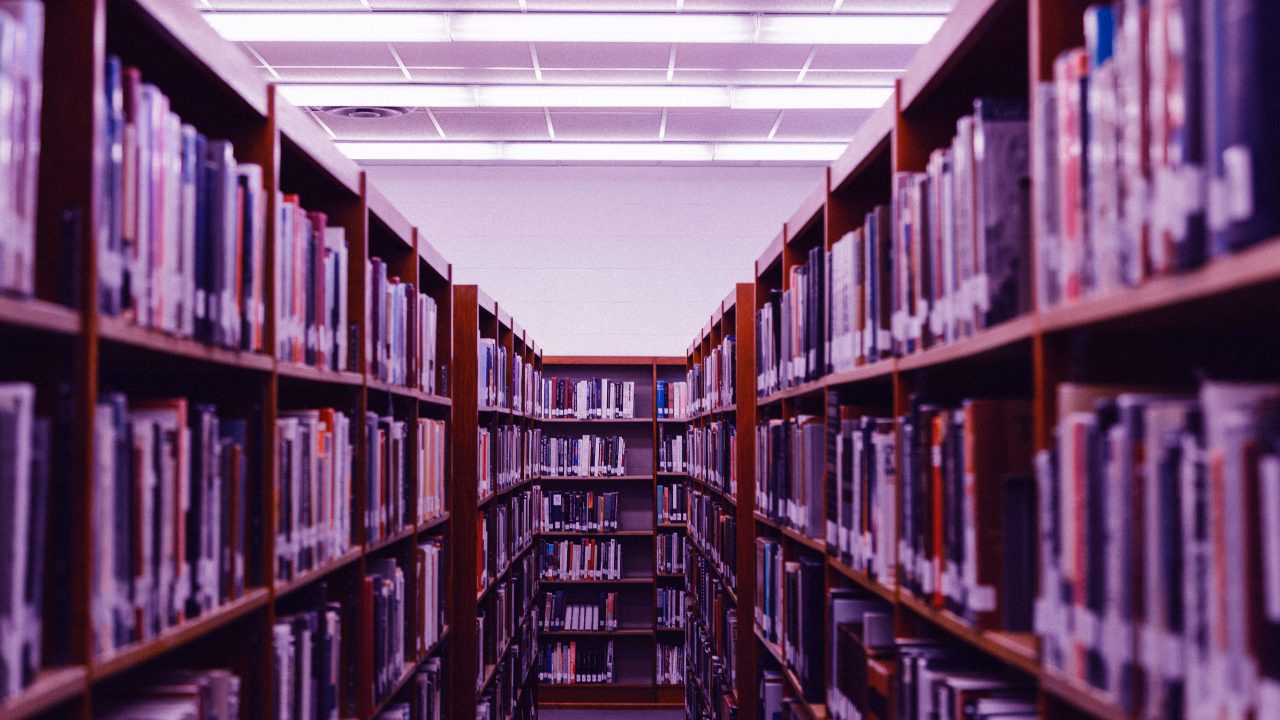 A photo of an aisle of books within a library, looking down with books on every shelf to the left and to the right