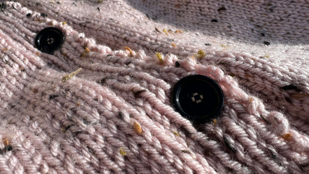 A close up of the knitted pink cardigan showing the pink tweed yarn and two black buttons