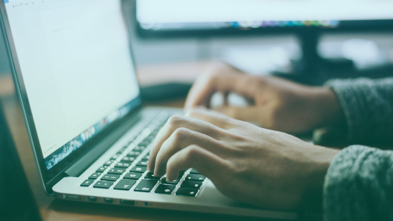 A photograph of hands typing on a Mac laptop