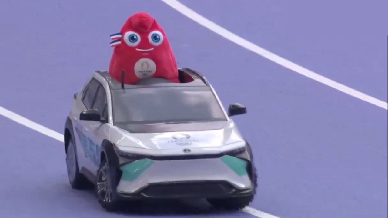 A still from live TV coverage of the Track & Field events where a stuffed Olympics 2024 mascot plushie is being remote control driven in a miniature javelin car