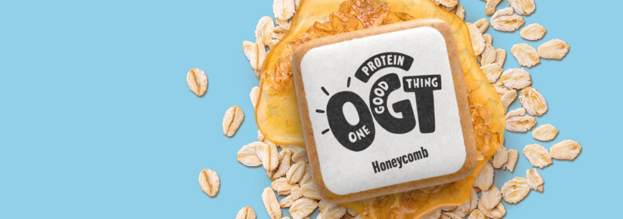 A marketing image of the One Good Thing wrapper-free protein bar, a square bar sitting on a bed of oats and honey