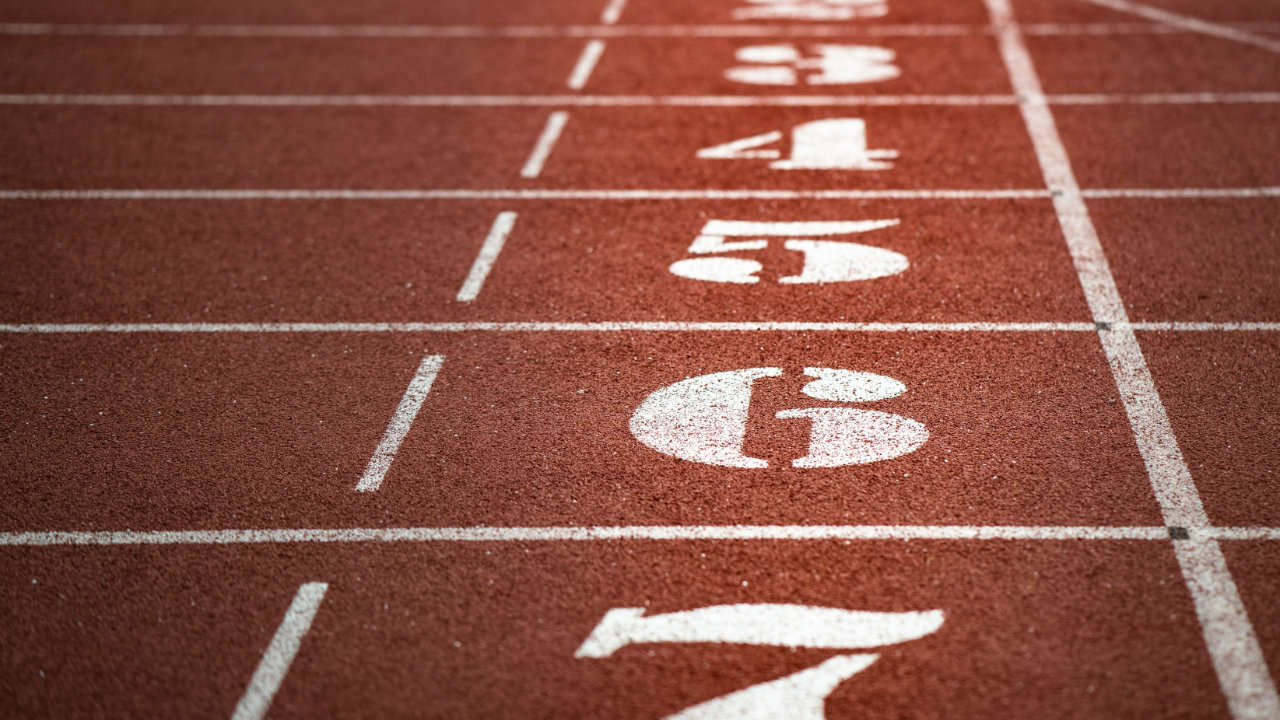 Looking sideways on the start/finish line of a red running track with the white painted numbers indicating each lane