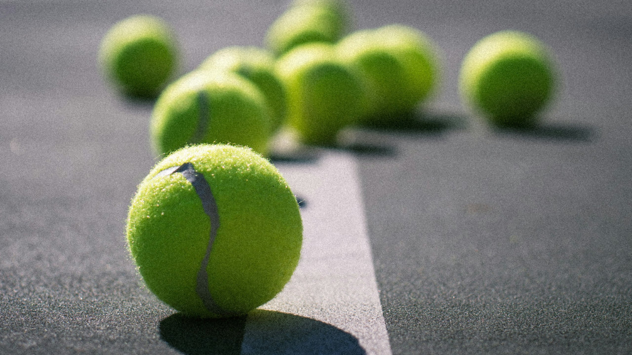 A photograph of a collection of tennis balls sitting on a tennis court, casting a shadow on the ground