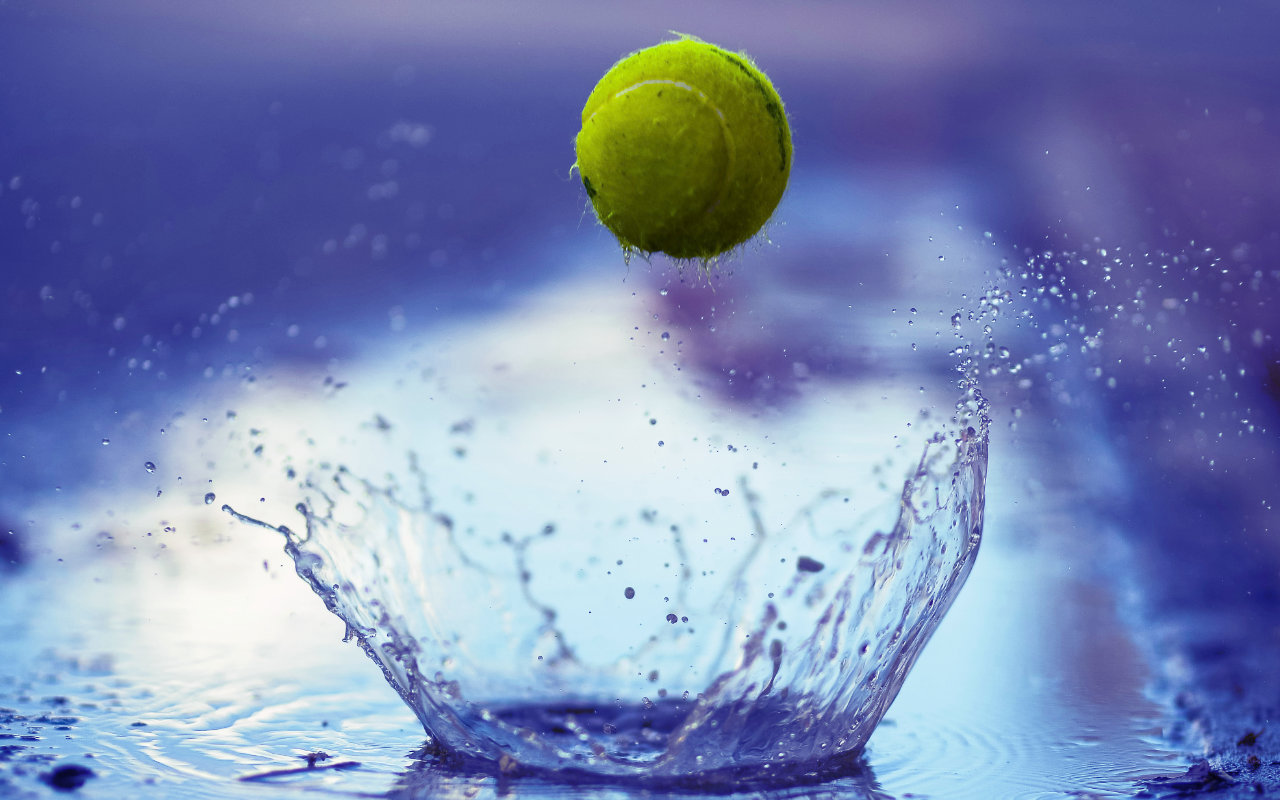 A tennis ball bounces on wet ground leaving a plume of water behind it