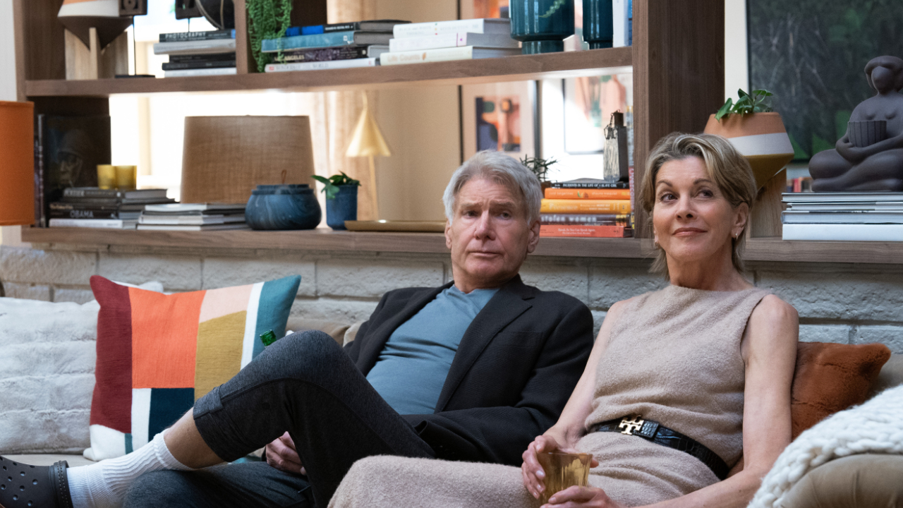 A still image from the second series of Shrinking featuring Harrison Ford as Paul and Wendie Malick as Julie, both sitting together on a living room sofa