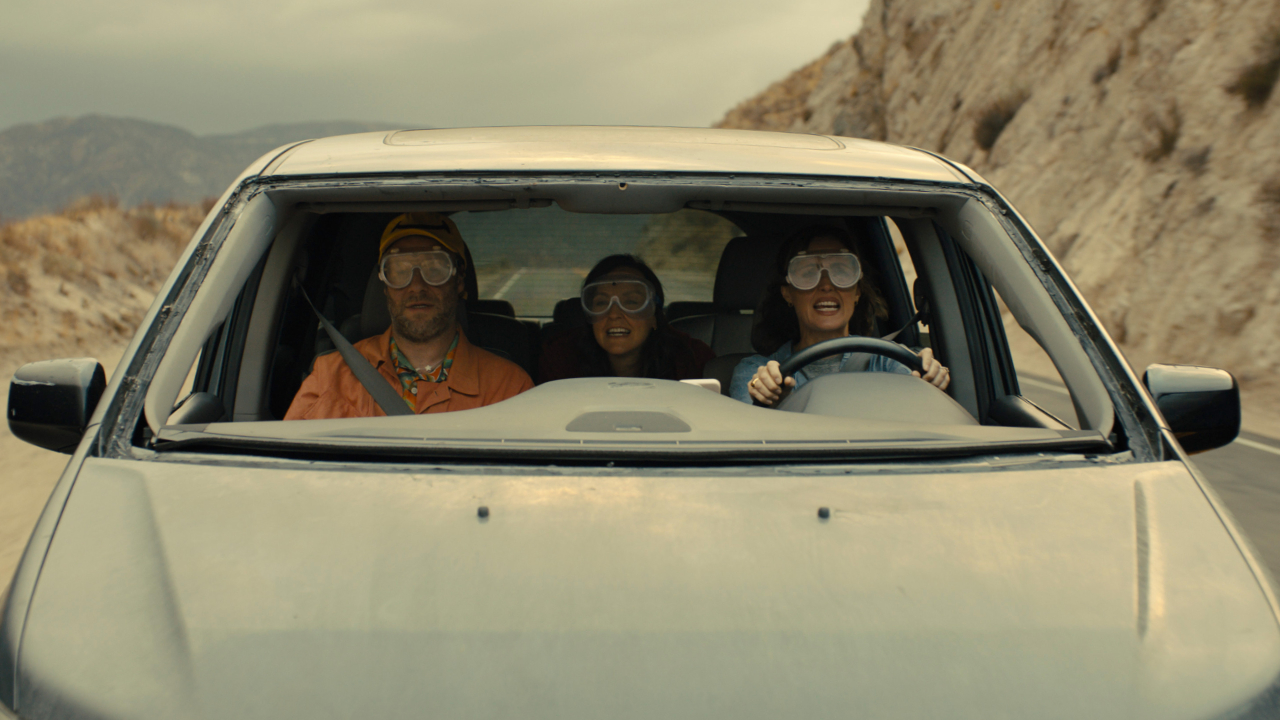 Rose Byrne and Seth Rogen in a still from the Apple TV show Platonic, driving a car with no windscreen and goggles on instead