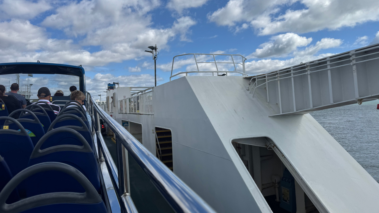 A photo from the top deck of an open top bus looking left to discover the bus is on a ferry boat over the water