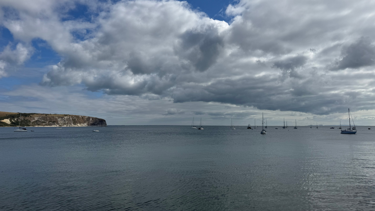 A photo of the coastline at Swanage, with cliffs to the left and the sea meeting the sky, all bathed in blue and sunshine