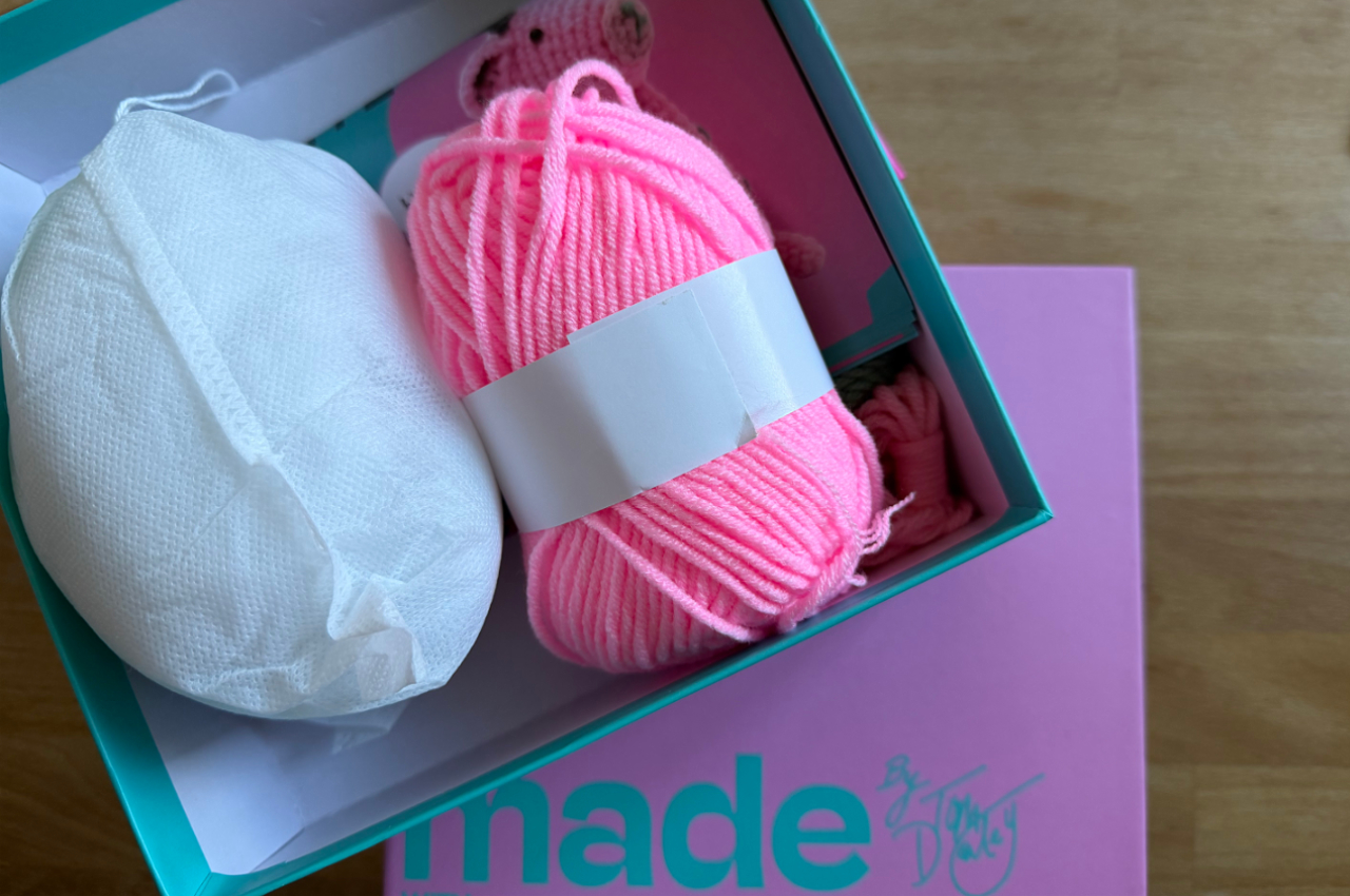 A photo of one of Tom Daley’s crochet kits, sitting open on a desk, with pink yarn, a ball of white toy stuffing, and instructions showing the pink giraffe that should be made by the end