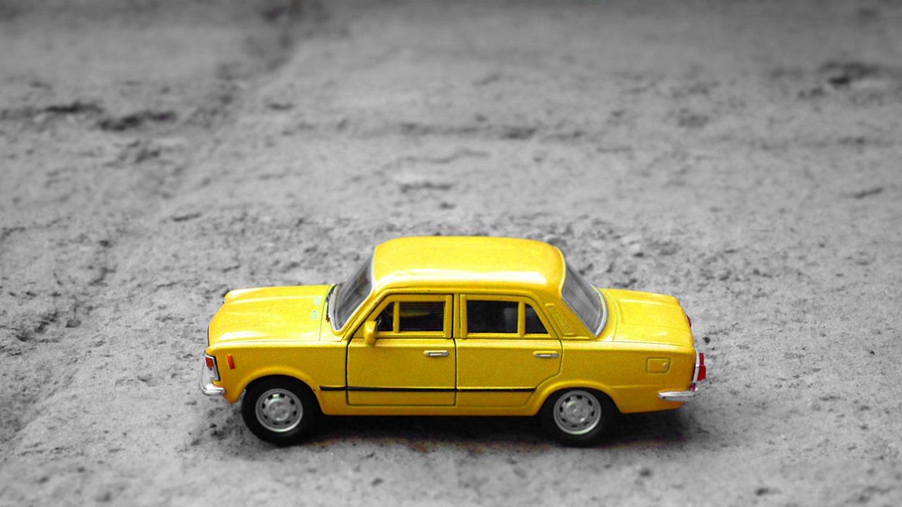 A toy yellow car sitting on a grey surface