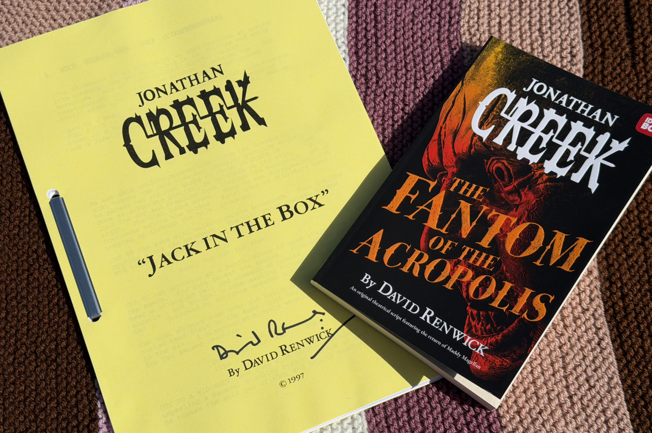 Sitting on a blanket, to the left a signed Jonathan Creek script with yellow cover from the episode &lsquo;Jack in the Box&rsquo; and to the right the new Jonathan Creek book called The Fantom of the Acropolis