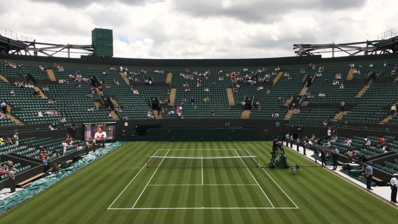 An old photo from Wimbledon Court No 1, looking out on an empty court, with mostly empty grandstands and a cloudy sky